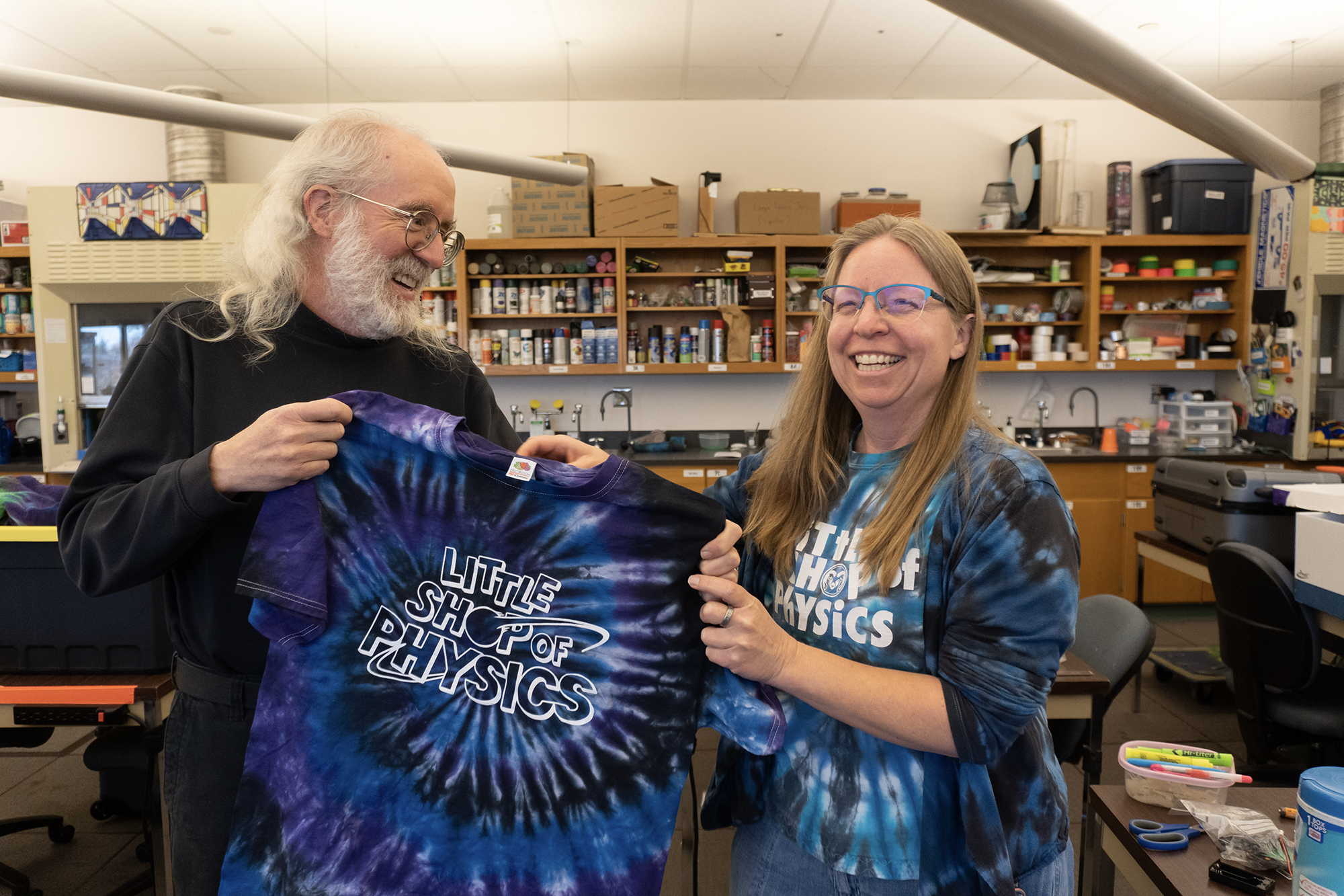 Brian Jones hands a tye-dyed shirt with the words "Little Shop of Physics" to Heather Michalak.